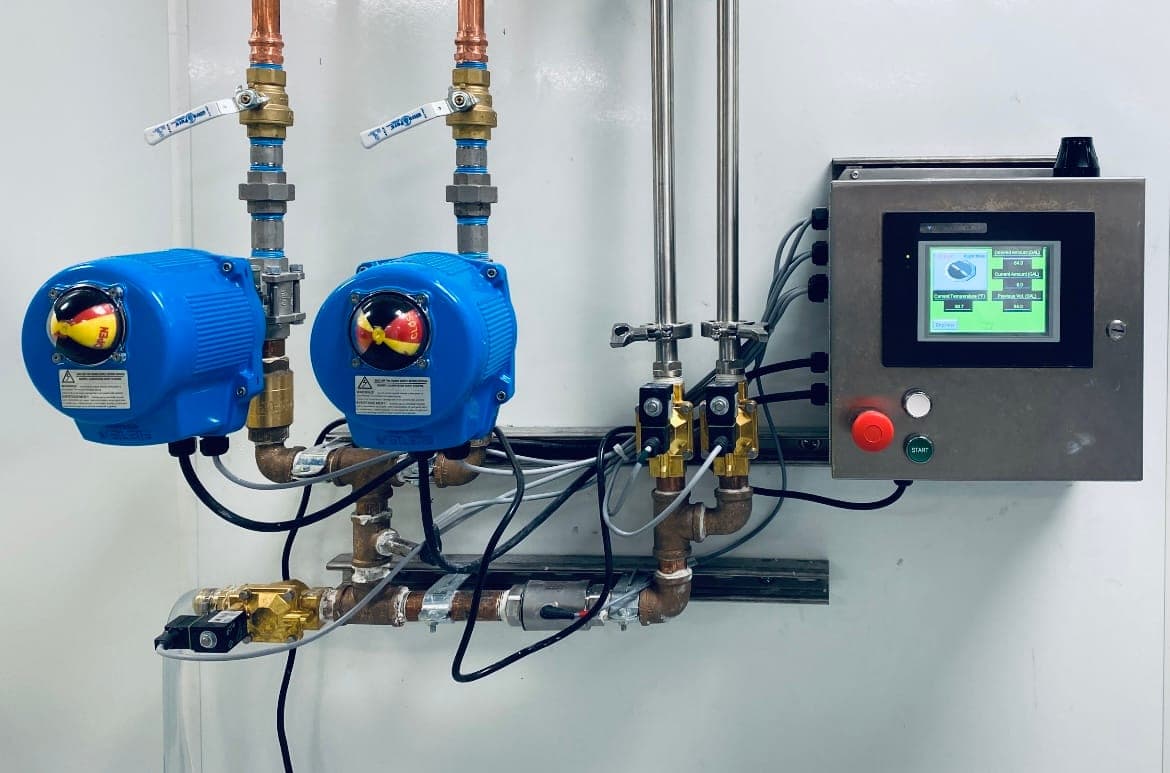 Actuated ball valves and copper piping feeding a stainless control enclosure with a touchscreen batching display