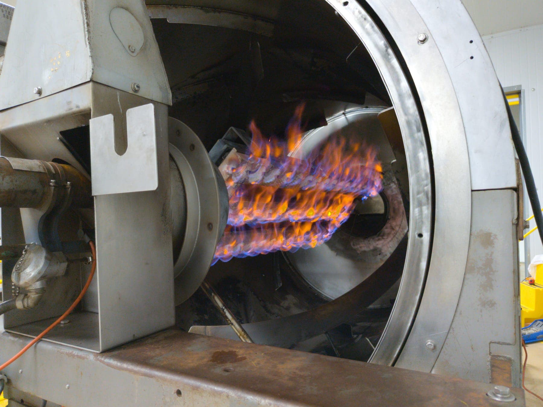 A ribbon burner firing inside a stainless rotary drum during process trials