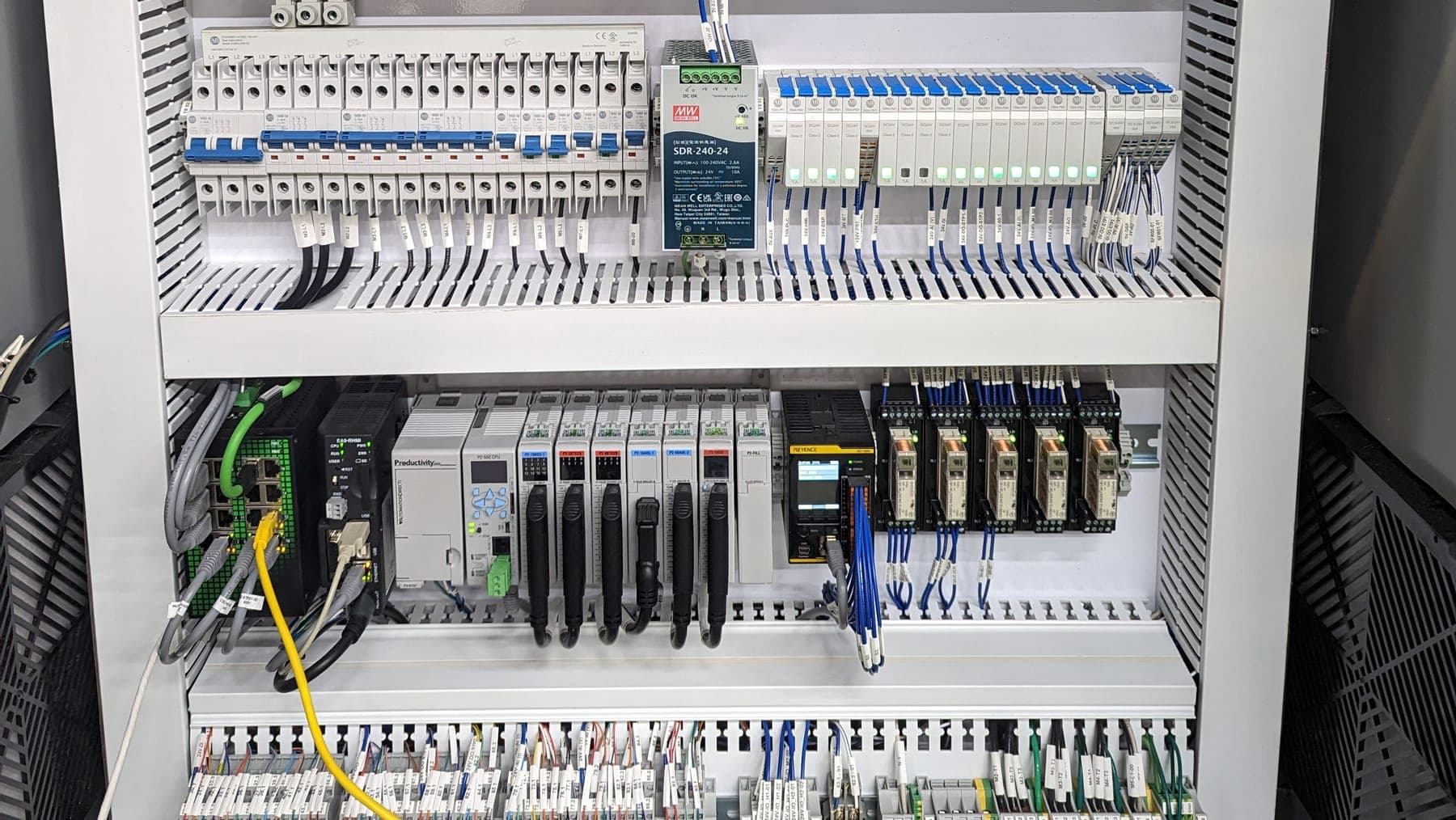Interior of a finished control panel — breakers, 24V supply, PLC with I/O cards, relays and fully labeled terminal blocks in dressed wire duct